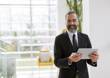 Ofiste çalışan, okuyan ya da bir şey arayan dijital tablet ile Yakışıklı gülümseyen olgun işadamı