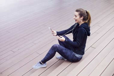 Genç, sportif bir kadın cep telefonu kullanıyor ve merdivenlerde oturuyor.