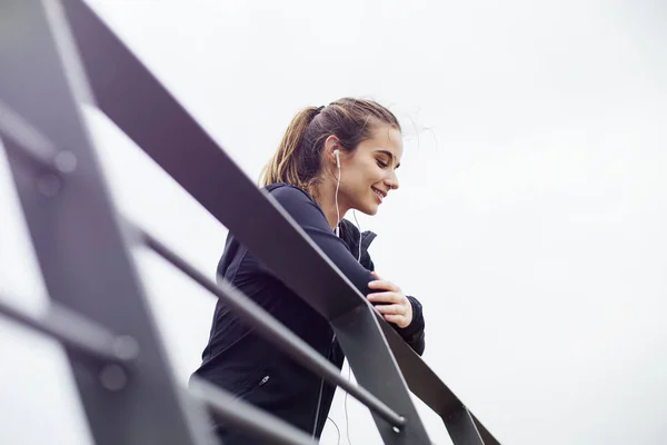 Mujer Joven Deportiva Con Auriculares Escuchando Música Apoyándose Valla Mirando —  Fotos de Stock