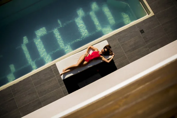 수영장 근처에서 휴식을 취하는 비키니에 선글라스를 착용한 아름다운 무두질 여성의 — 스톡 사진
