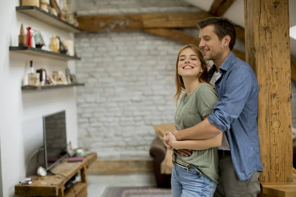 Genç bir adam ve bir kadın evlerinde durup birbirlerine sarılırlar ve kocaları karısına nazikçe sarılırlar.