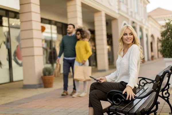 Hermosa Mujer Con Teléfono Móvil Sentado Banco Por Las Tiendas — Foto de Stock