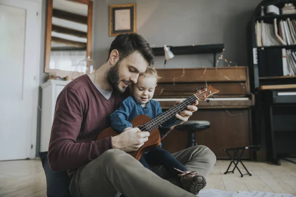 Dad shows the girl how to play the guitar in the room