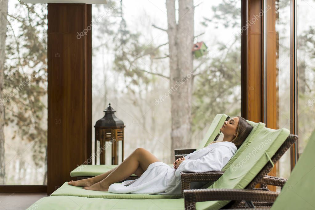 Pretty young woman relaxing on the deckchair by the swimming pool in spa