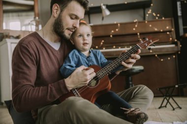 Babam kıza odada nasıl gitar çalacaklarını gösterir.