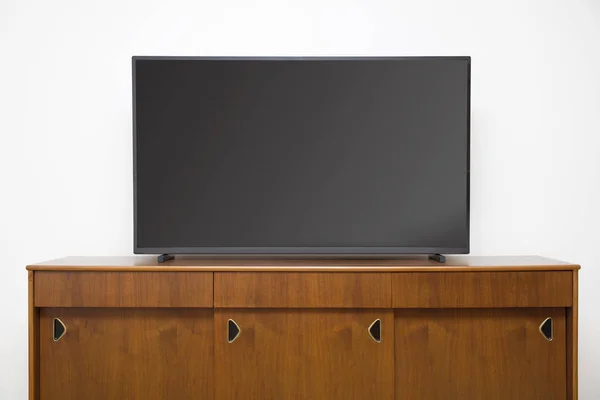 Modern TV set with empty blank screen on the wooden cabinet in front of white wall