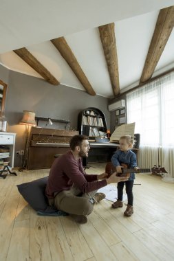 Genç baba odada yerde otururken gitar çalmak için onun sevimli küçük kızı öğretim