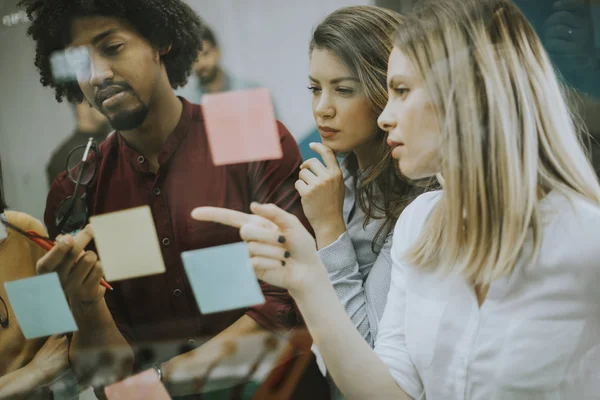 Group of young business people discussing in front of glass wall using post it notes and stickers at startup office