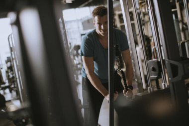 Genç yakışıklı sportif adam spor salonunda pull-down makine üzerinde çalışıyor