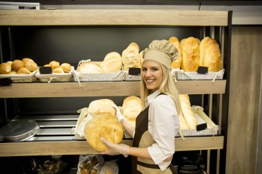 Pretty young woman selling soft  fresh bread in the bakery clipart