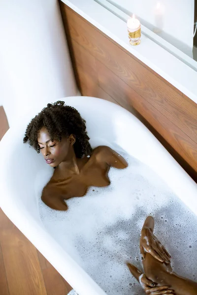 Beautiful young african american woman bathing in a tub full of foam