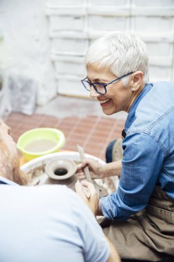 Çömlekçilik sınıfındaki bir öğretmenin yardımıyla çamurda dönen yaşlı bir kadın.
