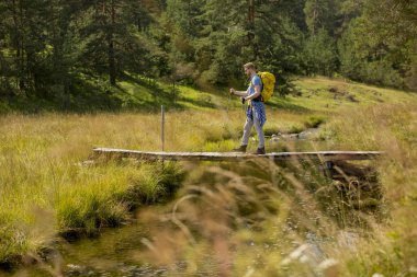 Sırt çantası ile Yakışıklı genç adam güneşli bir günde bir dağ dere haçlar