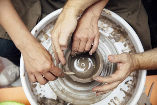 Çömlekçilik sınıfında bir öğretmenin yardımıyla bir tekerlek üzerinde kil dönen kıdemli kadın üst görünümü