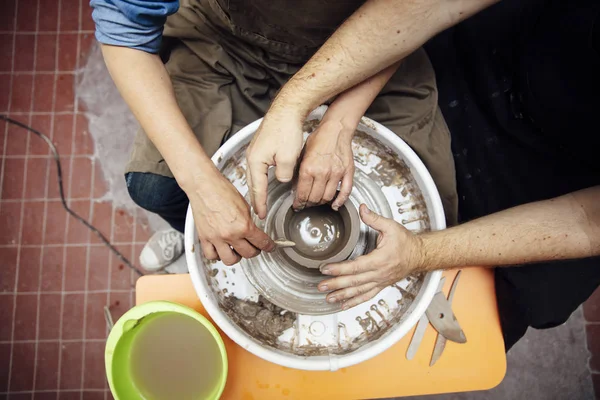 Çömlekçilik sınıfında bir öğretmenin yardımıyla bir tekerlek üzerinde kil dönen kıdemli kadın üst görünümü