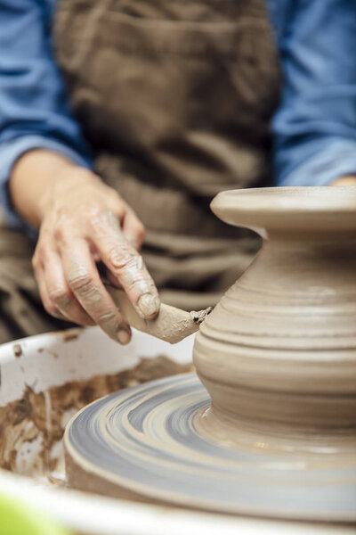 Close up detail view at an senior female artist makes clay pottery on a spin wheel