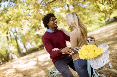 Güz parkında bisikleti olan çok ırklı genç bir çift.
