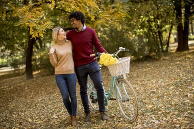 Güz parkında bisiklet süren çok ırklı genç bir çift