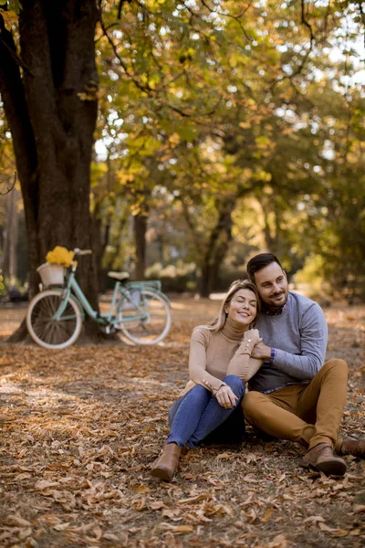 一对年轻夫妇坐在秋天公园的地上 — 图库照片