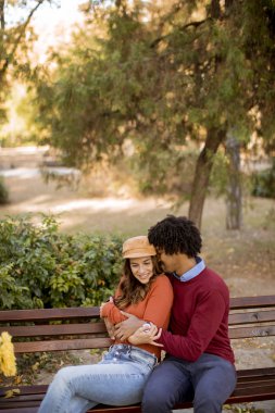 Sonbahar parkında bankta oturan çok yönlü, genç bir çift.