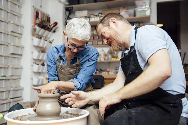 在陶瓷课上 在一位老师的帮助下 一位老妇人在轮子上旋转粘土 — 图库照片