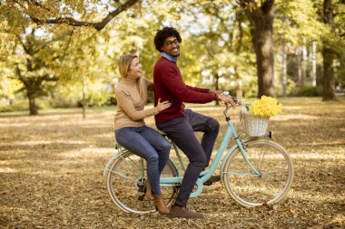 Sonbahar parkında bisiklet süren çok ırklı genç bir çift.