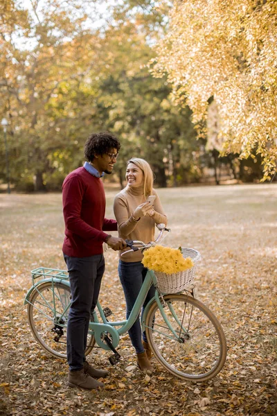 Молодая Многорасовая Пара Велосипедом Стоящая Осеннем Парке Пользующаяся Мобильным Телефоном — стоковое фото