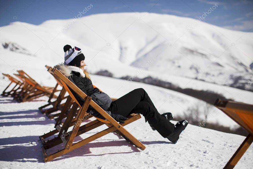 Young woman skier relaxing in a lounge chair after skiing in the mountains in winter