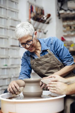 Çömlekçilik sınıfındaki bir öğretmenin yardımıyla çamurda dönen yaşlı bir kadın.