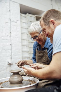 Çömlekçilik sınıfındaki bir öğretmenin yardımıyla çamurda dönen yaşlı bir kadın.