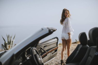 Yazın deniz kenarındaki beyaz atlı aracın yanında güzel bir genç kadın.