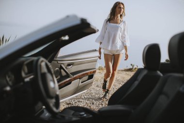 Yazın deniz kenarındaki beyaz atlı aracın yanında güzel bir genç kadın.