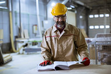 Handsome middle aged worker in protective clothes checking documentation in the factory