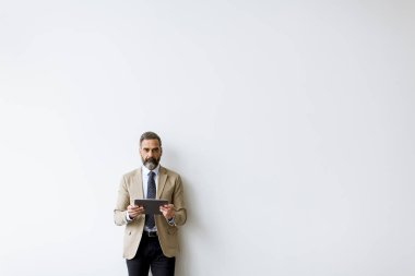 Handsome senior businessman with digital tablet standing by the wall