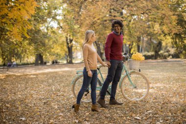 Güz parkında bisikleti olan çok ırklı genç bir çift.