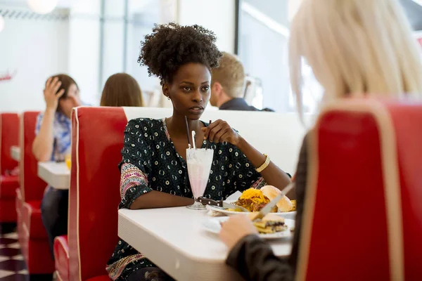 Multiracial young female friends eating fast food at a table in the diner