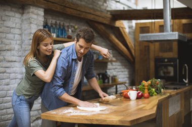 Neşeli genç çift birlikte kırsal mutfakta pizza yapıyor.