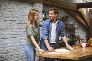 Neşeli genç çift birlikte kırsal mutfakta pizza yapıyor.