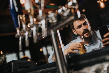Genç adam bira içiyor, sigara içiyor ve barda cep telefonu kullanıyor.