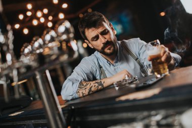 Gece kulübünde bira içip sigara içen genç bir adam.