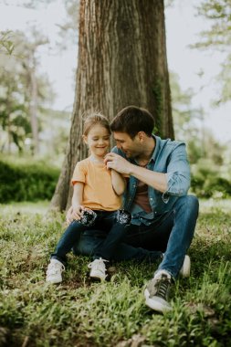 Bekar bir baba ağaçta çimlerin üzerinde oturuyor, yanında da küçük tatlı bir kızı var.