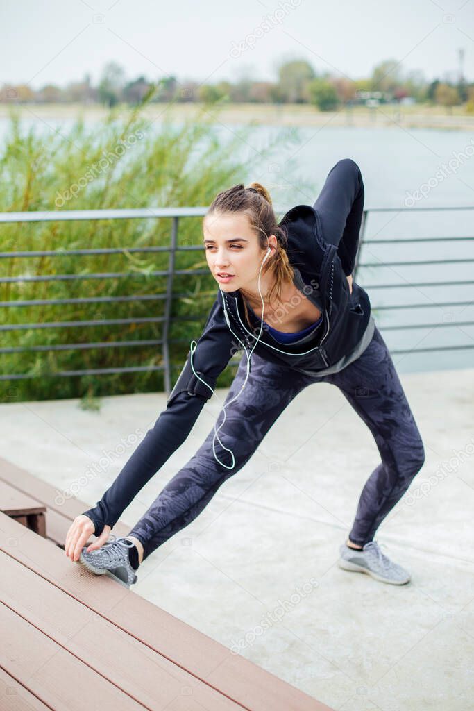 Fit young woman with earphones doing stretching exercises on urban stairs outdoors