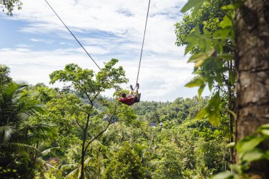 Genç erkek turist Endonezya 'daki tropik bir Bali adasının yağmur ormanında uçurumda sallanıyor. Ormandaki uçurumda sallanan genç turist kadın