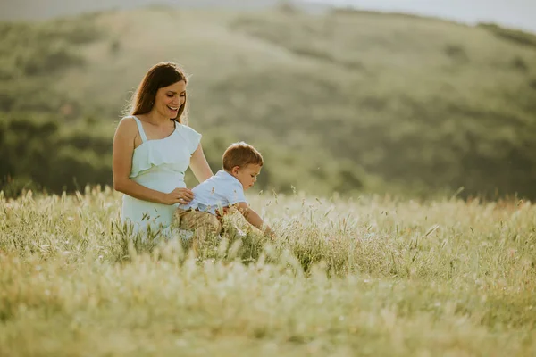 若いです妊娠中のお母さんとともに彼女の可愛いです男の子でフィールドで美しい夏の日 — ストック写真