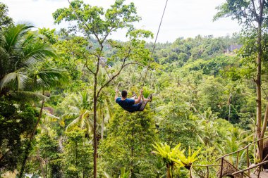 Genç erkek turist Endonezya 'daki tropik bir Bali adasının yağmur ormanında uçurumda sallanıyor. Ormandaki uçurumda sallanan genç turist kadın