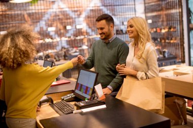 Elbise dükkanında kredi kartıyla kadın satış asistanı ödeyen yakışıklı bir genç.