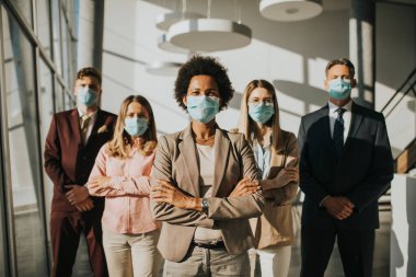 Bir grup Asyalı iş adamı ofiste duruyor ve Corona virüsü bulaşmasını önlemek için maske takıyor.