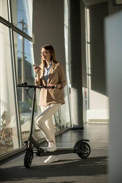 Mujer Bastante Joven Pie Junto Ventana Oficina Con Scooter Eléctrico — Foto de Stock