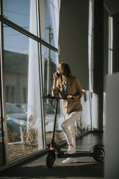 Wanita Muda Cantik Berdiri Dekat Jendela Kantor Dengan Skuter Listrik — Stok Foto