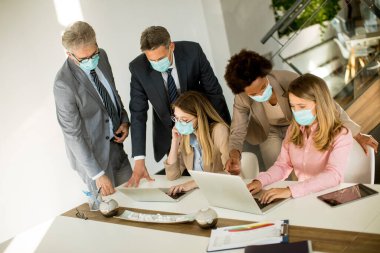 Grup iş adamlarının ofiste bir toplantısı var ve Corona virüsünden korunmak için maske takıyorlar.